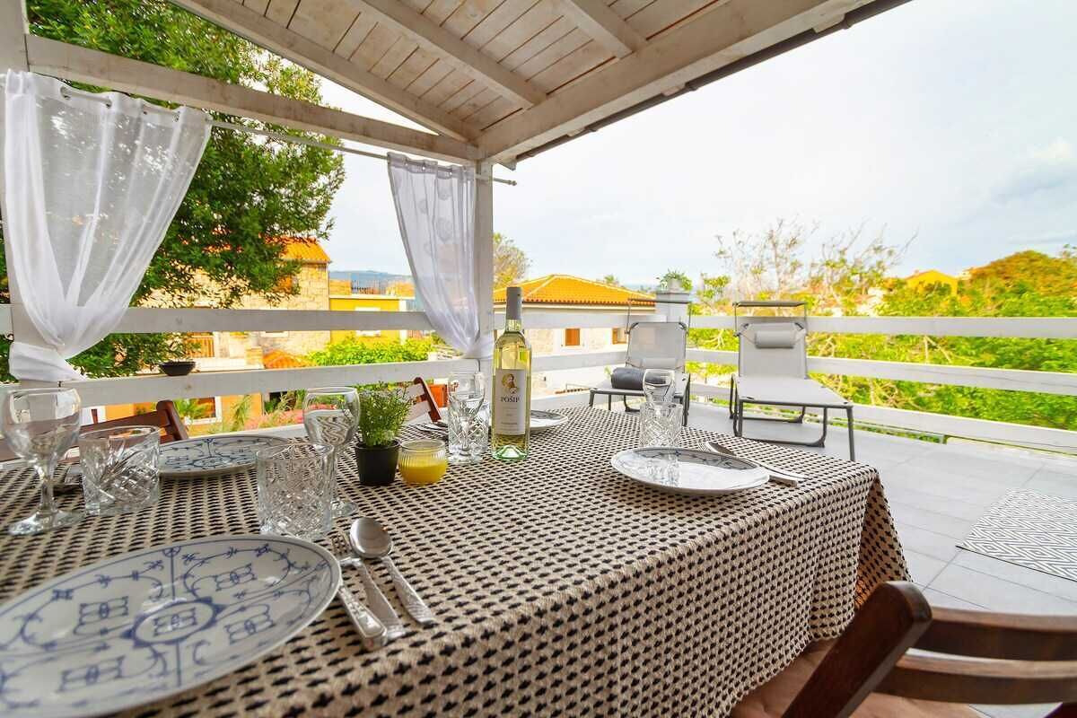 An outdoor dining area with a table set for two, a bottle of wine, and a view of the surrounding landscape.