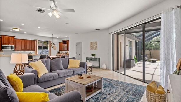 A modern living room with a grey sofa, a coffee table, and a view through large sliding glass doors to an outdoor patio. - Family Friendly 3BR Beach House with salt water heated pool (Englewood)