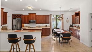 A modern kitchen with wooden cabinets, a stainless steel refrigerator, and a dining area with a large island and bar stools. - Family Friendly 3BR Beach House with salt water heated pool (Englewood)