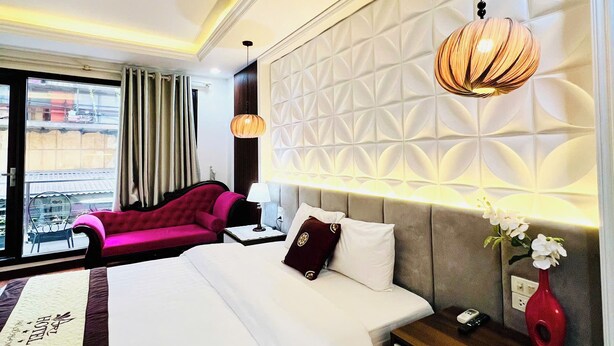 A hotel room with a bed, a nightstand, a red vase, and a view of the outside. - Art Hotel Ha Noi (Hanoi)