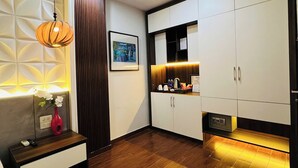 A modern hotel room with a wooden floor, a bedside table with a vase, a hanging light fixture, a framed picture on the wall, and a wardrobe with a built-in shelf. - Art Hotel Ha Noi (Hanoi)