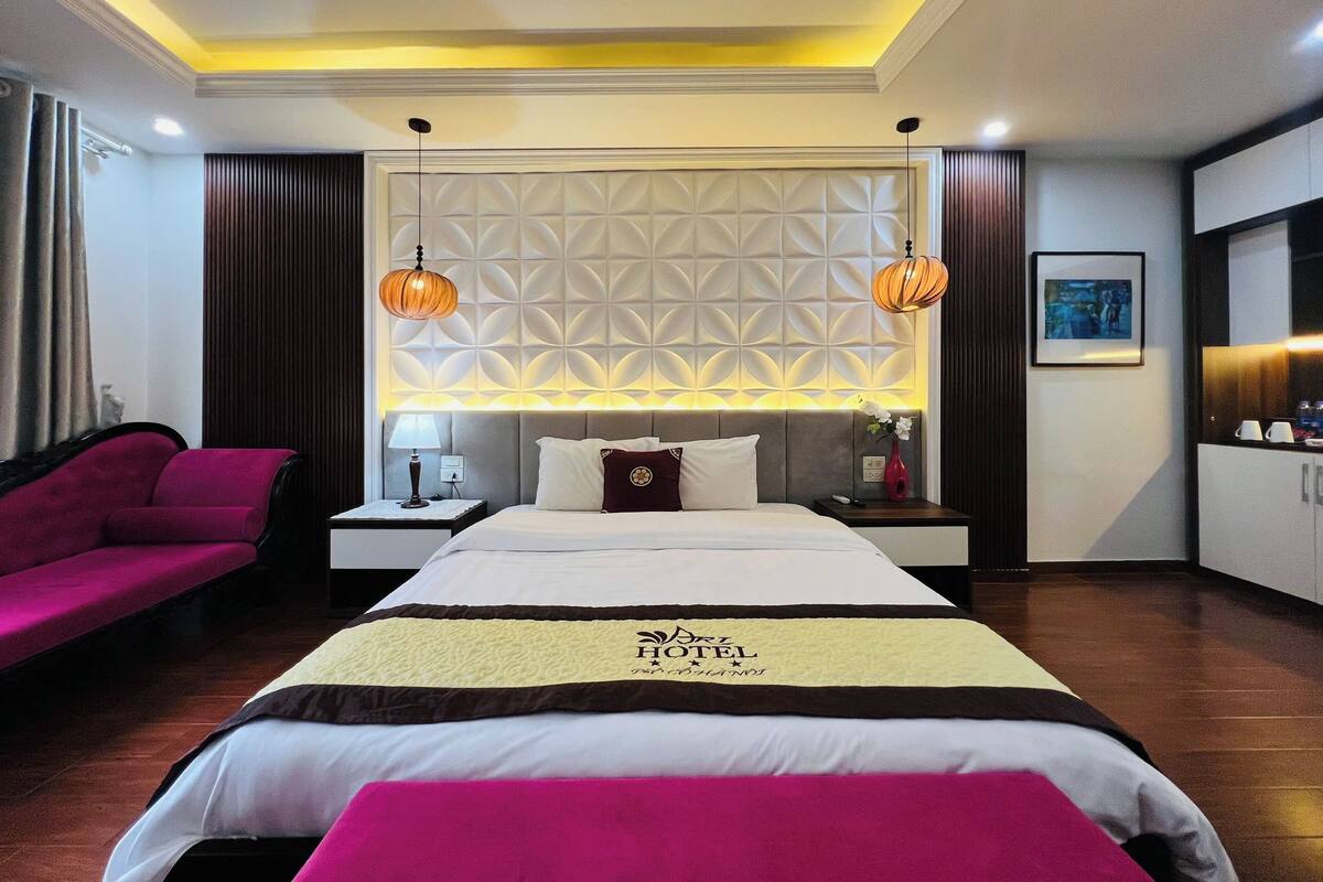 Una habitación de hotel con una cama grande, una mesita de noche, una lámpara, una silla roja y una pared con un diseño geométrico.