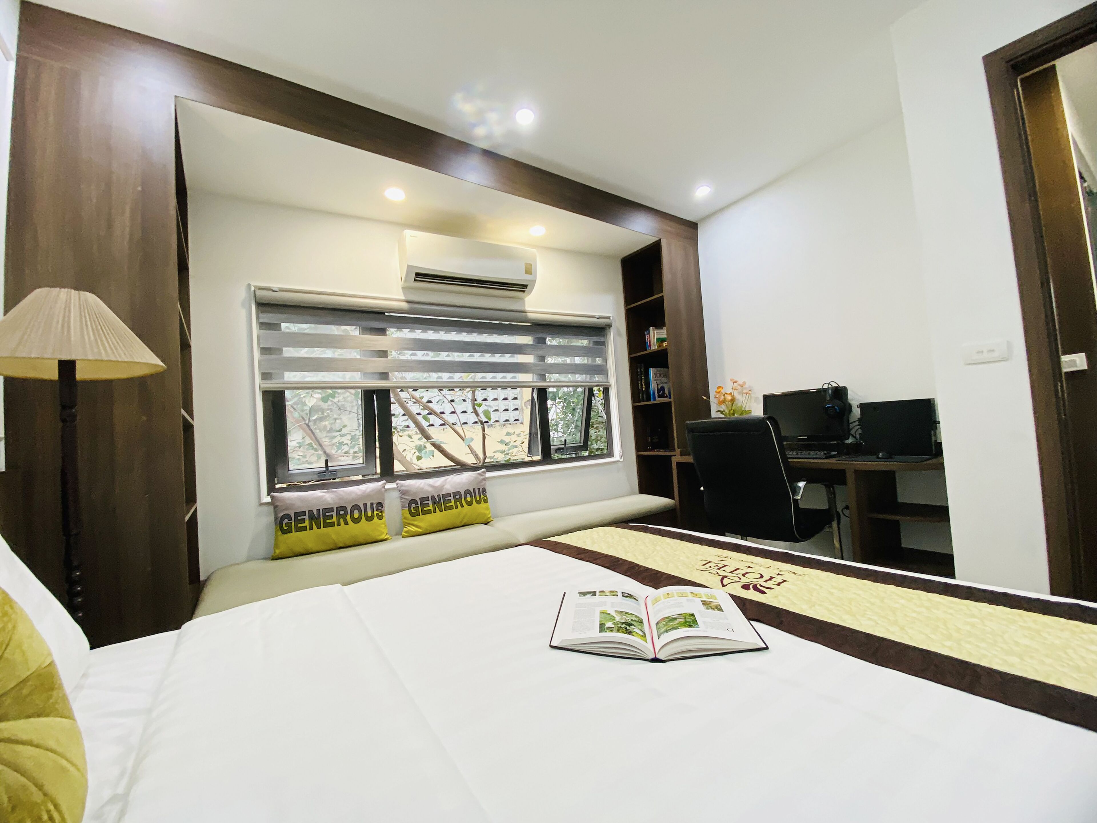 A hotel room with a bed, a desk, a chair, and an air conditioning unit.