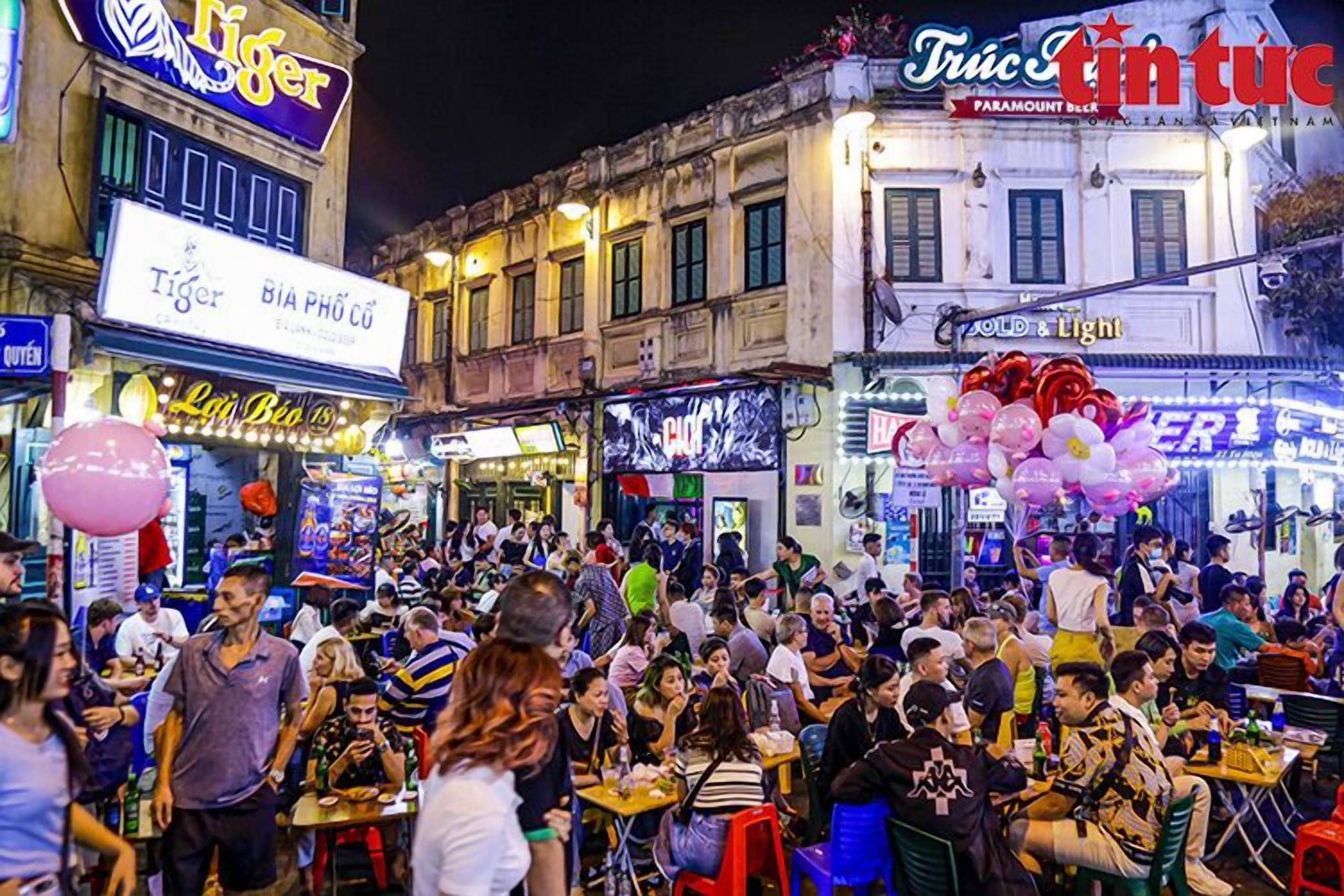 A crowded street scene with various shops and signs, including 'Tiger' and 'Truc Tien Tuc'.
