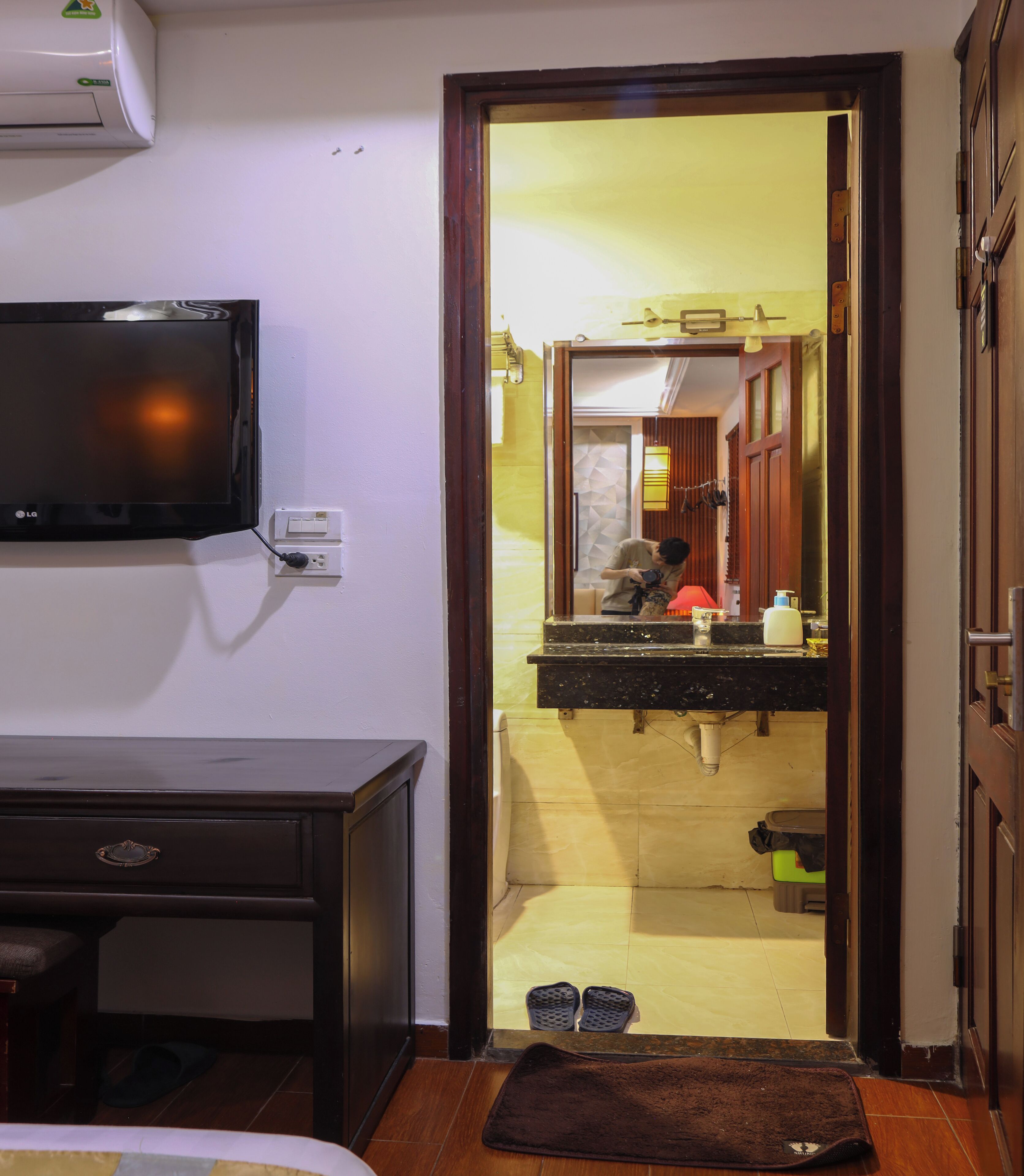 Habitación de hotel con televisor montado en la pared, un escritorio, un espejo y una puerta que da a un baño.