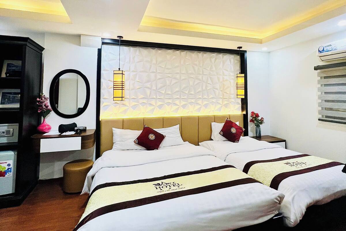 Una habitación de hotel con una cama grande, una mesita de noche, un espejo y una lámpara fijada a la pared.