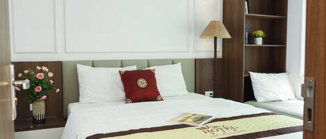 Una habitación de hotel con una cama, una mesita de noche con un jarrón de flores, una lámpara y una estantería.