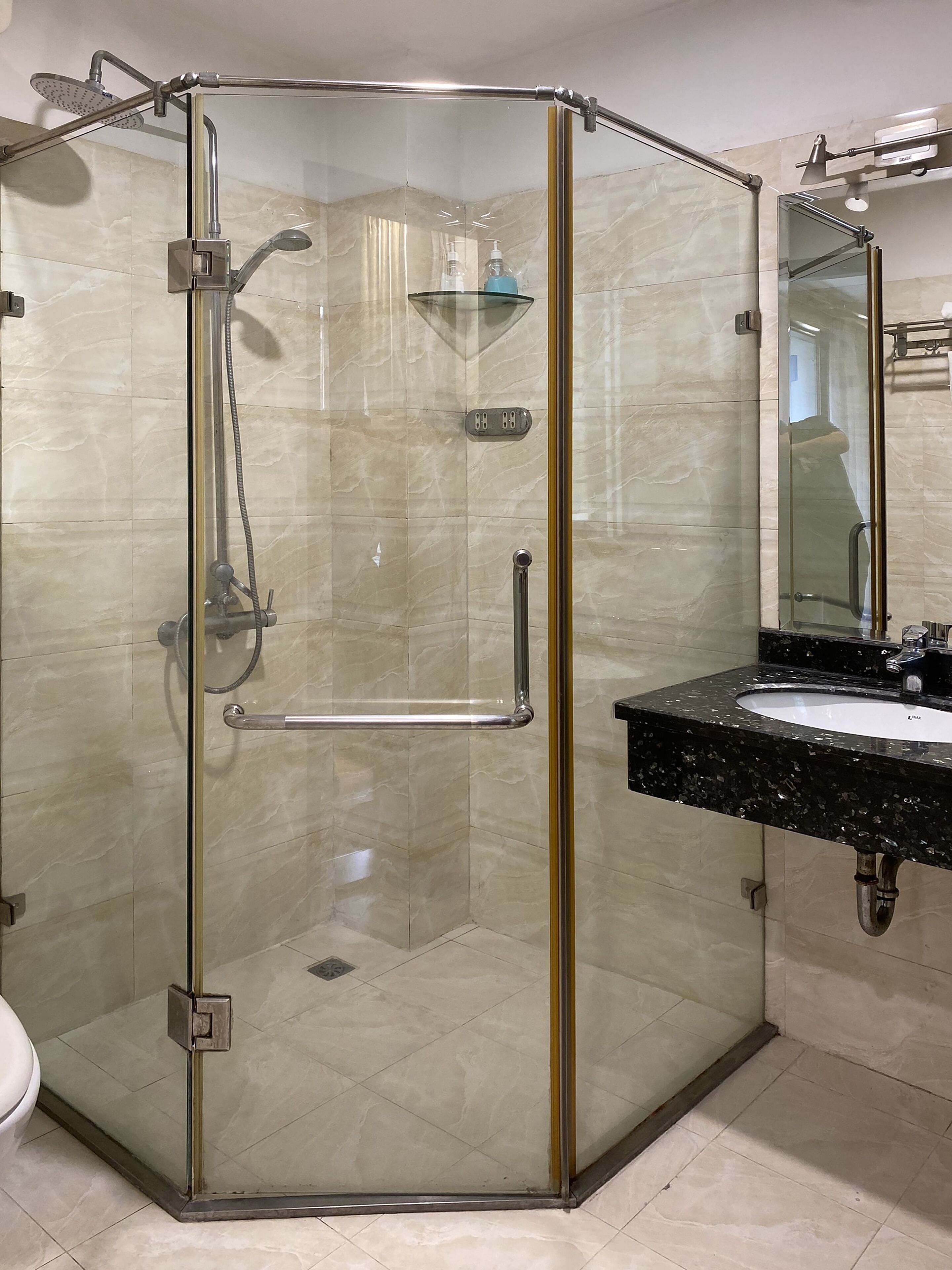 Une douche fermée par des parois en verre, dotée d’un pommeau de douche à main et d’un robinet à main.