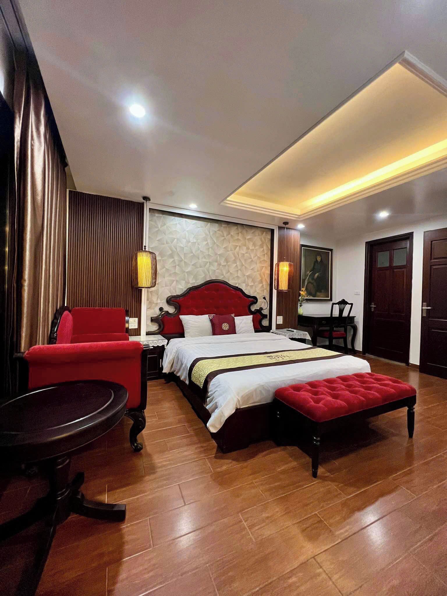 Une chambre d’hôtel moderne avec un grand lit, un fauteuil rouge, une petite table ronde et un banc en bois.