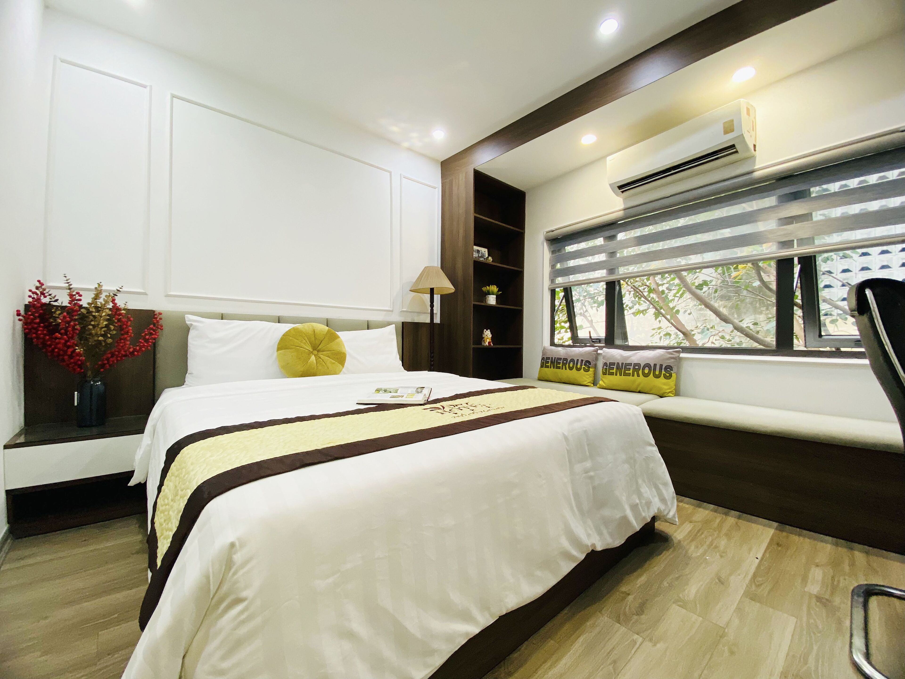 Una habitación de hotel ordenada con cama, mesita de noche, lámpara y ventana con persianas.