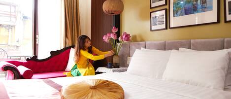 Une chambre d’hôtel avec un lit, un canapé rouge, un vase rempli de fleurs roses et des tableaux encadrés accrochés au mur.