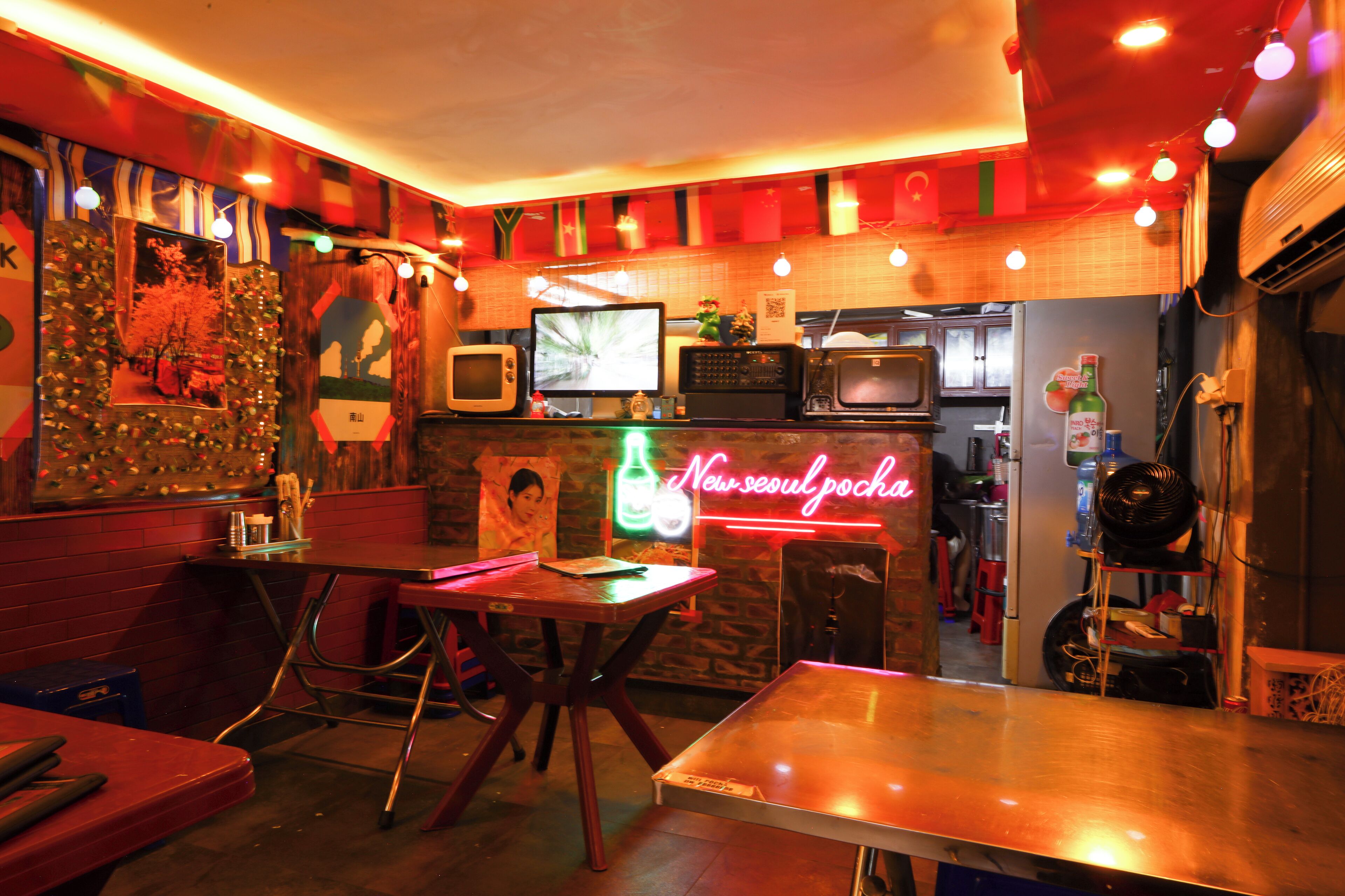A restaurant with a neon sign, tables, chairs, and a counter with a TV.