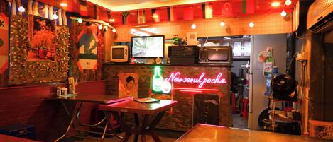 A restaurant with a neon sign, tables, chairs, and a counter with a TV.