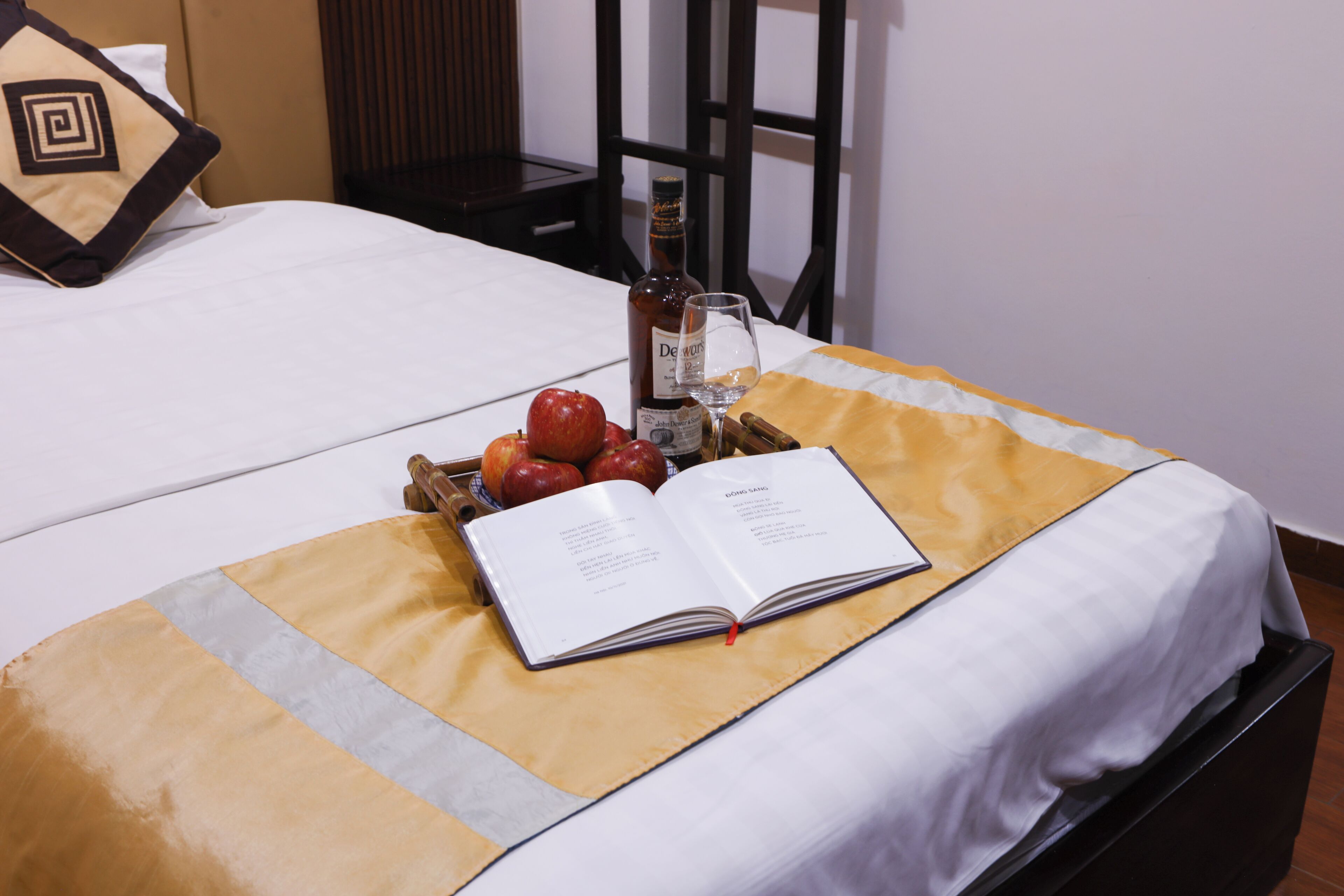 Un lit bien fait, avec un livre, une bouteille et un bol de fruits posés sur le couvre-lit.
