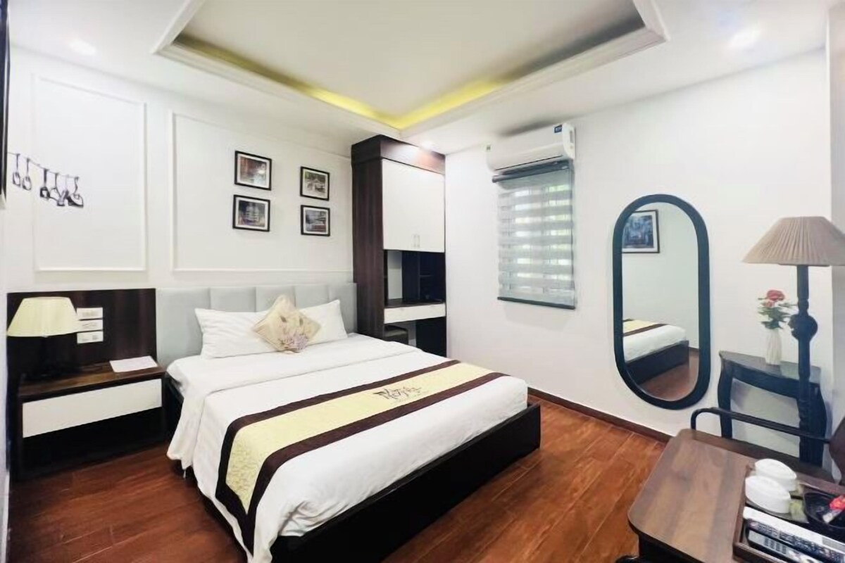 A hotel room with a bed, bedside tables, a mirror, and a window with blinds.