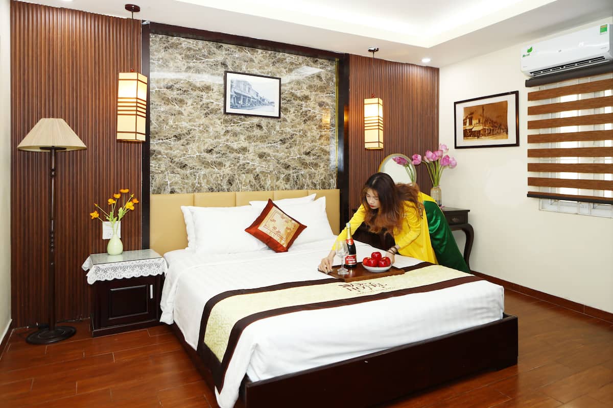 Una habitación de hotel con una cama, una mesita de noche, una lámpara, un jarrón con flores y un cuadro en la pared.