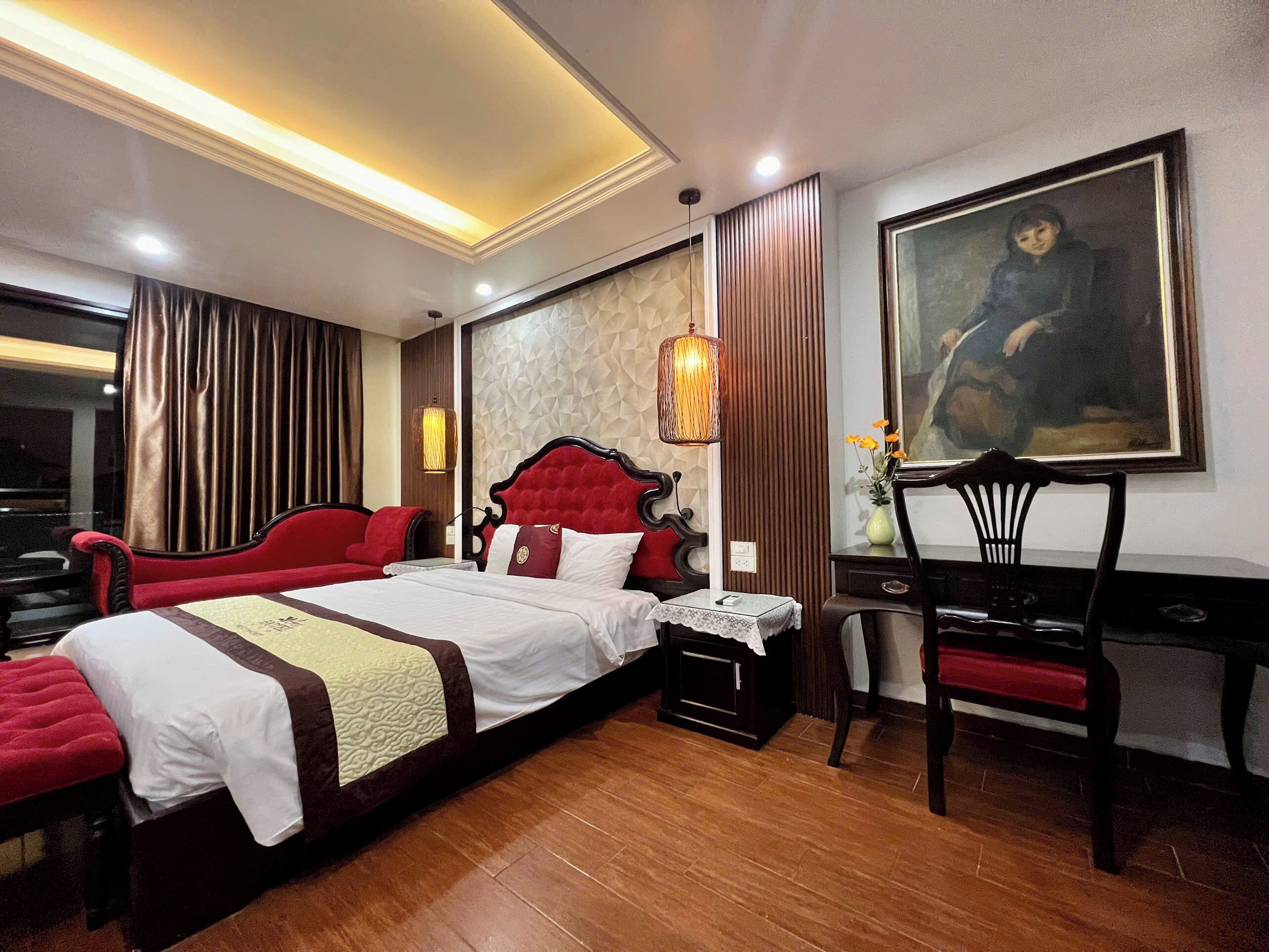 A hotel room with a large bed, a desk, a chair, and a painting on the wall.