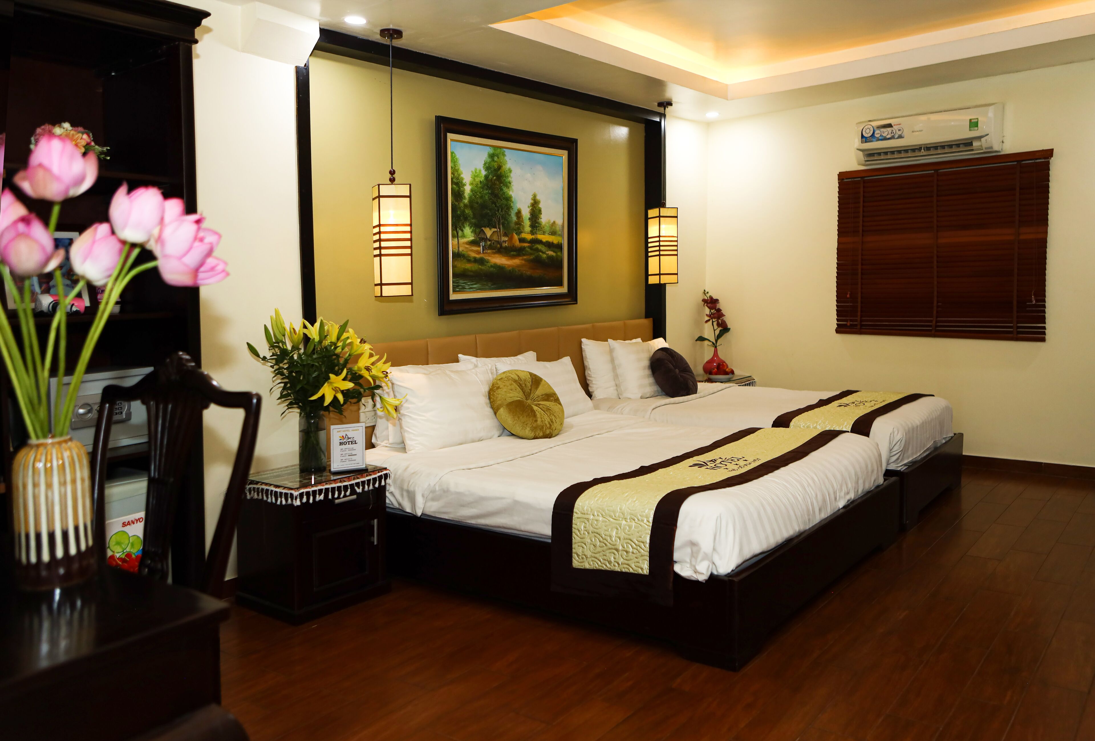 A hotel room with a large bed, a painting on the wall, and a desk with a vase of flowers.