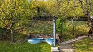 A garden with a swimming pool, a stone wall, and a wooden fence.