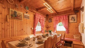 A wooden dining room with a table set for four, wooden chairs, and checkered curtains.
