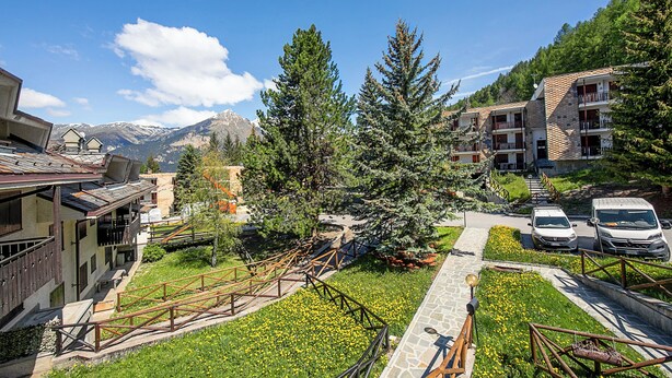 Un hotel con fachada de piedra, varios balcones y vistas a montañas nevadas.