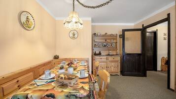 Un espace repas avec une longue table dressée pour le repas, des chaises en bois, un lustre et une porte donnant sur une autre pièce.