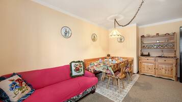 Un salon chaleureux avec un canapé rouge, une table à manger avec des chaises et un coin cuisine doté de meubles en bois.