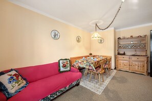 Una sala de estar acogedora con un sofá rojo, una mesa de comedor con sillas y una zona de cocina con armarios de madera.