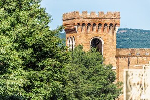Une tour historique en briques, dotée de fenêtres en arc de cercle, et entourée d’une végétation luxuriante.