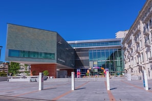 A modern building with a glass facade, a stone facade, and a plaza with a seating area.