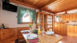 Una mesa de madera para comer con platos, cubiertos y una jarra de jugo. Hay un banco de madera y un televisor montado en la pared.
