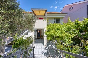 A residential building with a staircase leading to a door, surrounded by greenery and a clear sky.