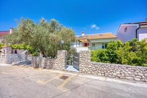 A residential street with stone walls, a clear blue sky, and a house with a tiled roof.