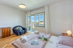 A bedroom with a bed, a wooden wardrobe, a dark blue sofa, a window with a view, and a lamp on the bedside table.