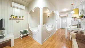 Una habitación con una cama, un escritorio, una silla y un televisor. Hay estantes con plantas y una mesita con una planta.