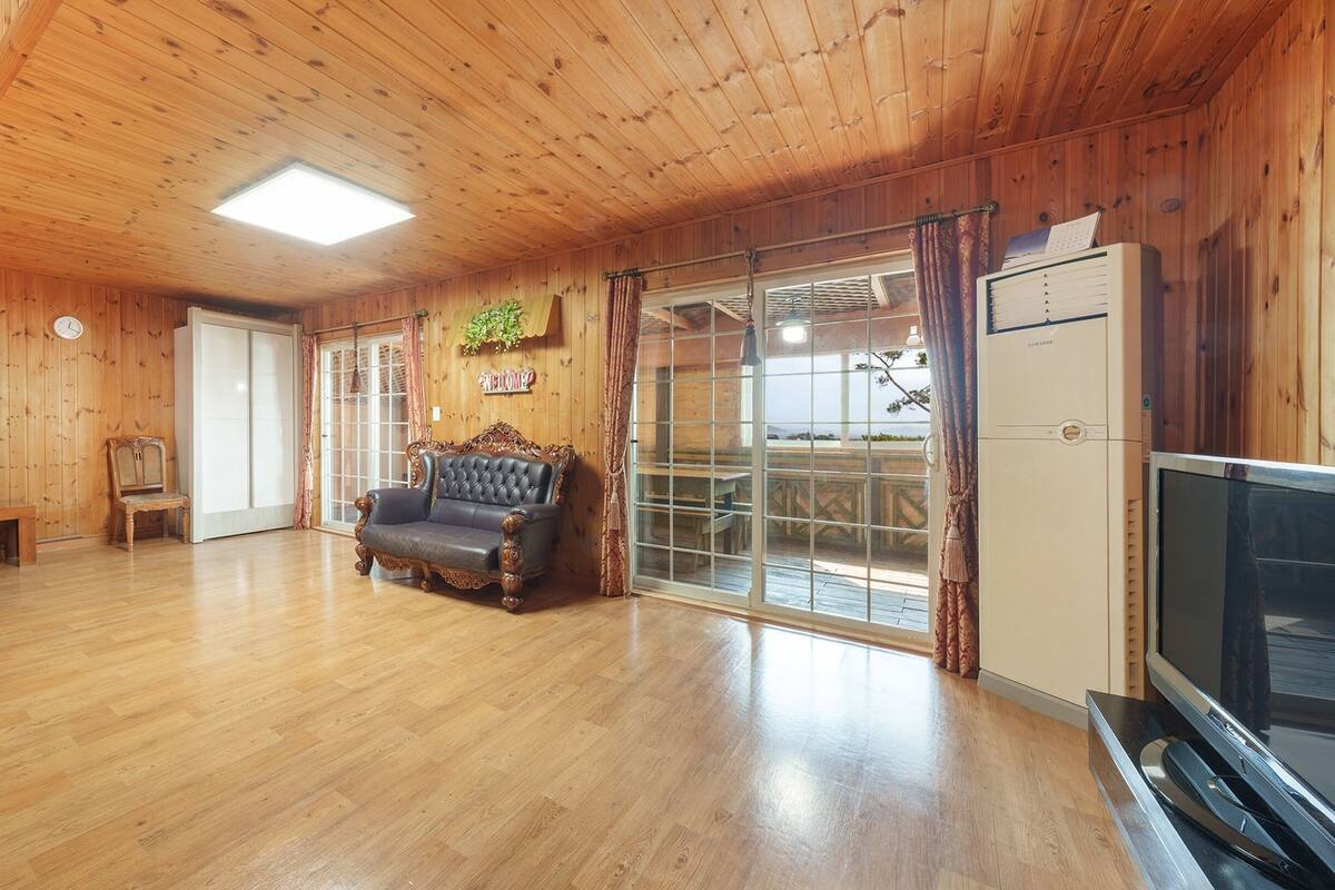 A wooden interior with a sofa, a television, and a sliding glass door leading to an outdoor area.