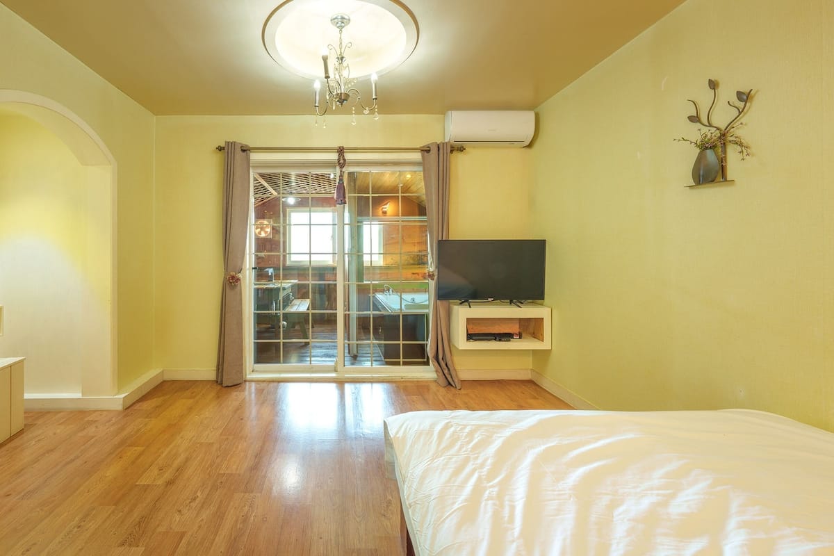 A bedroom with a bed, a TV, a sliding glass door, and a wooden floor.