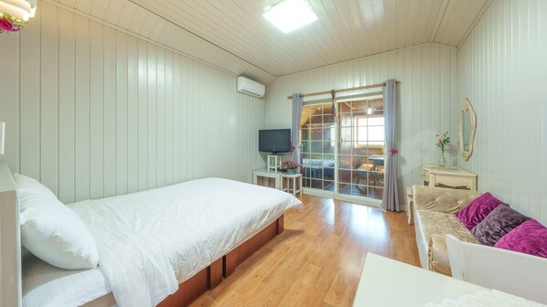 A bedroom with a bed, a TV, a small table with a vase, and a sliding glass door leading to a balcony.