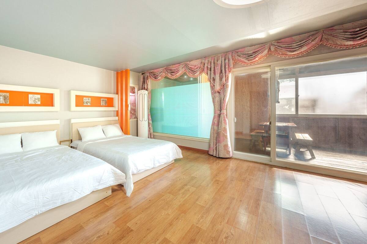 A hotel room with two beds, a large window with curtains, and a sliding glass door leading to an outdoor area.