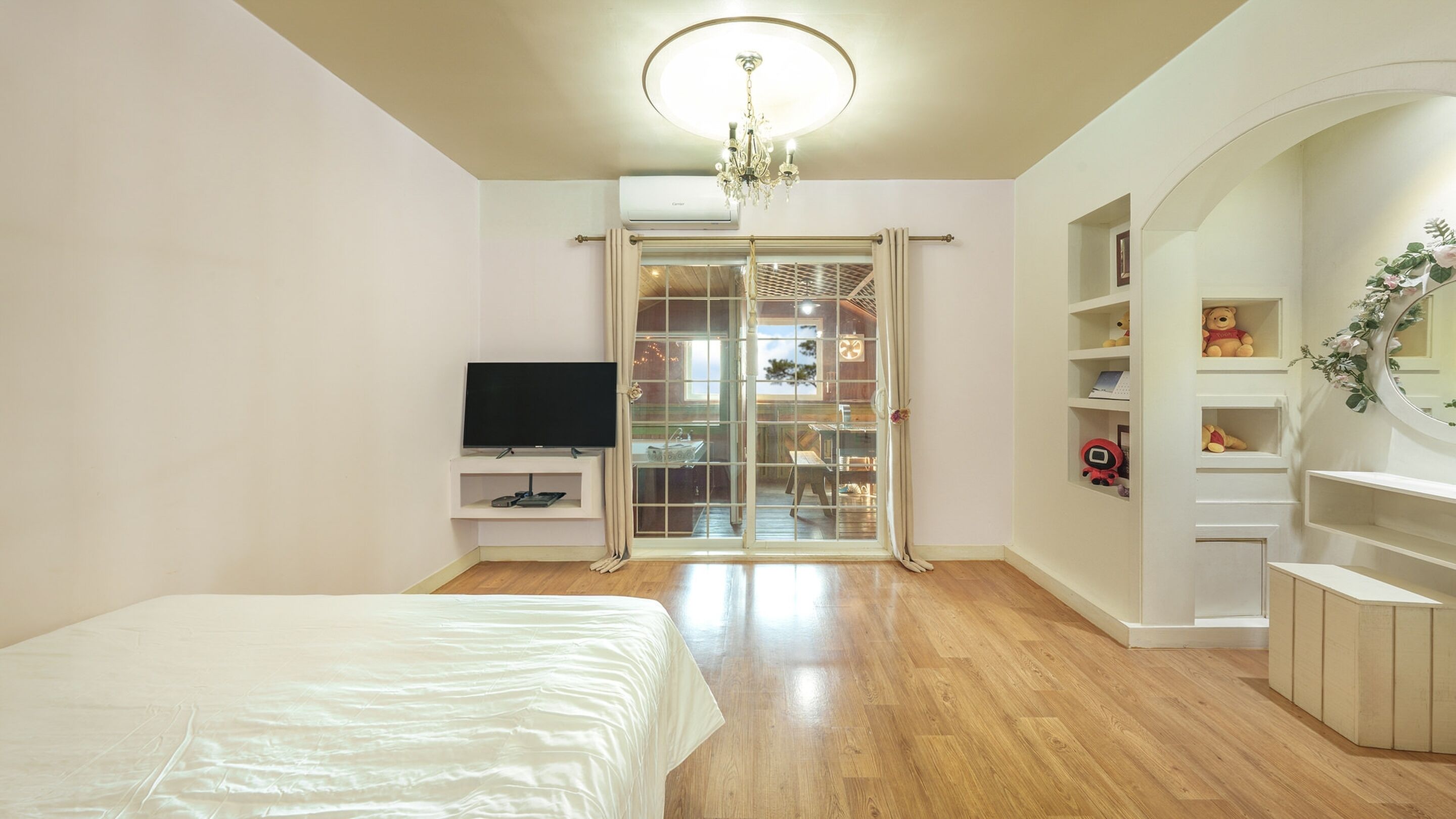 A bedroom with a bed, a TV, a sliding glass door to a balcony, and a built-in bookshelf.