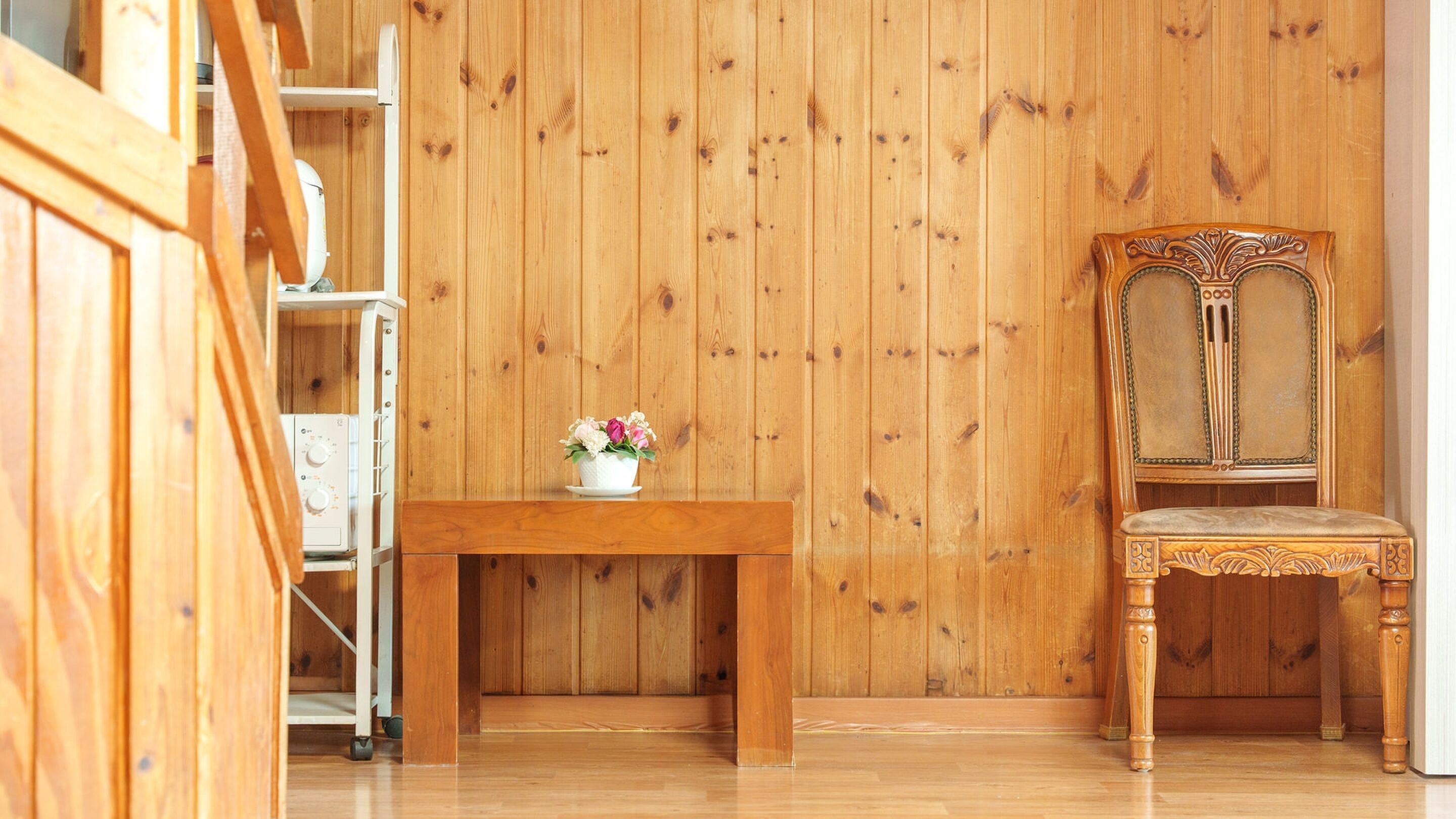 Una habitación con paredes de madera, una mesa de madera con un florero y una silla de madera.