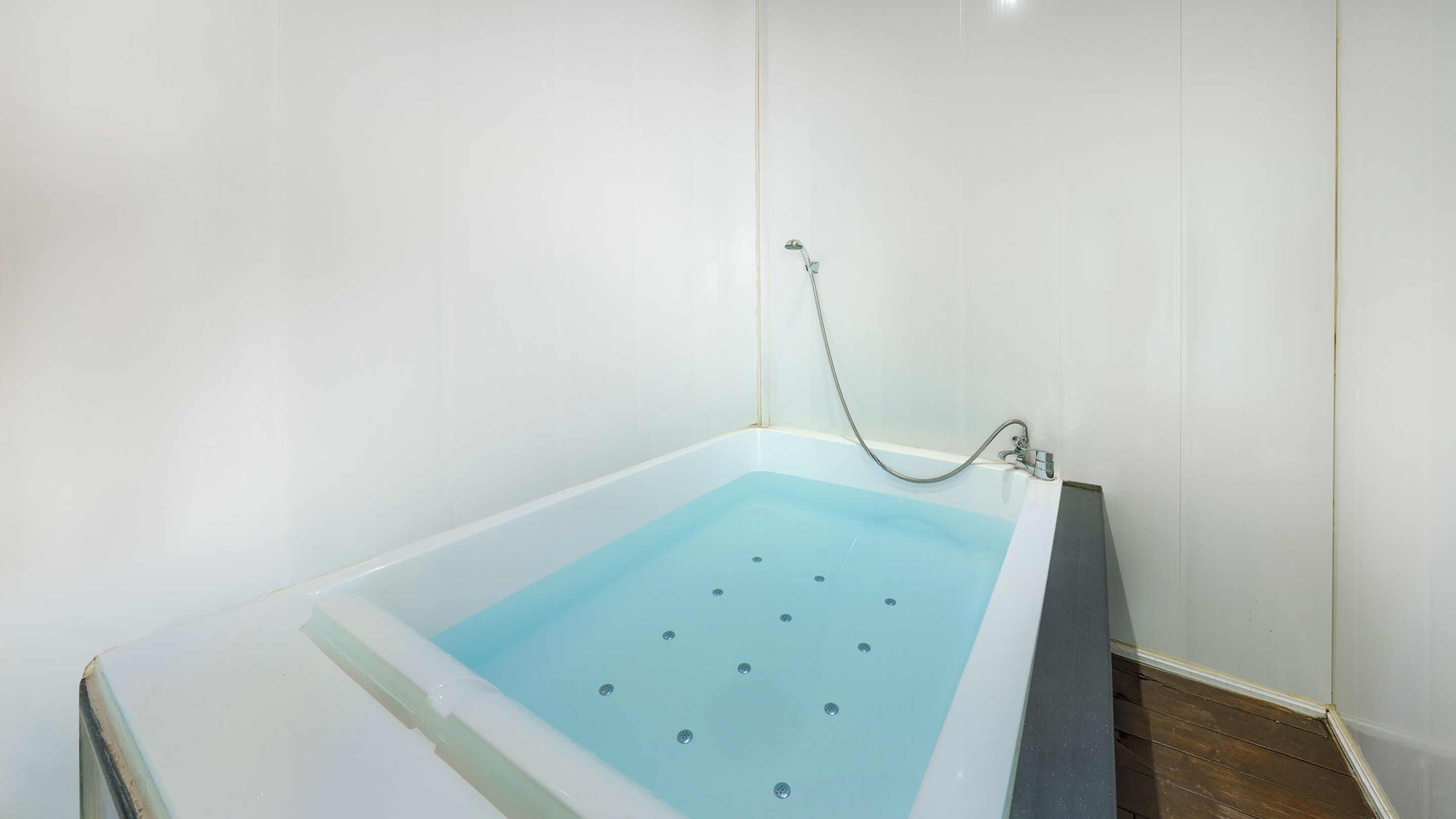 Una bañera con ducha, pared de azulejos blancos y suelo de madera.