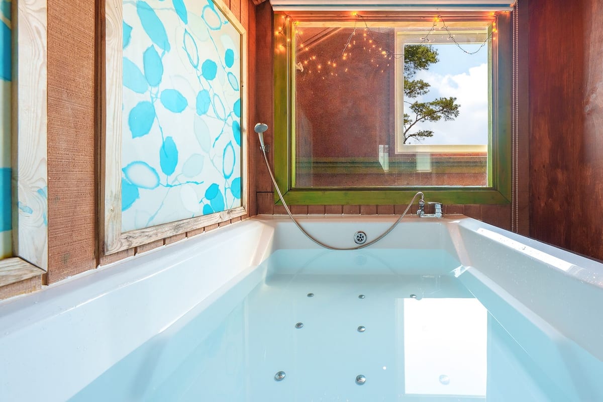 A bathroom with a large bathtub, a shower, and a window with a view of trees.