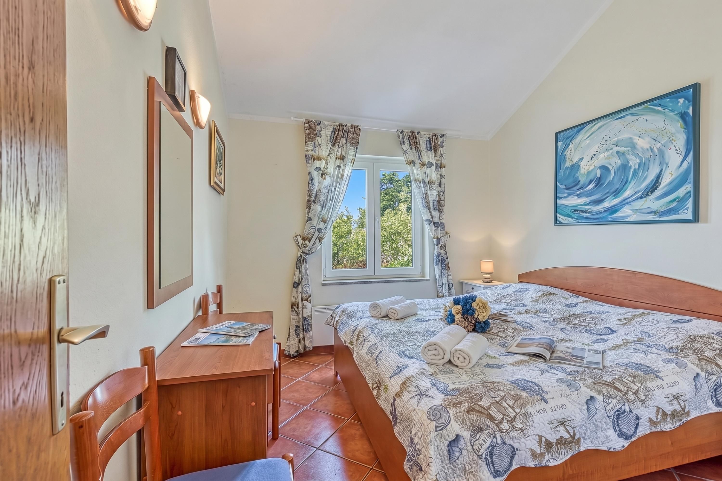 Une chambre à coucher avec un lit, un bureau, une chaise, une fenêtre avec des rideaux et un tableau au mur.