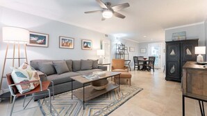 Un salon comprenant un canapé, une table basse et un fauteuil, un coin repas avec une table et des chaises, et un ventilateur de plafond.