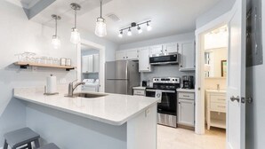 Une cuisine moderne dotée d’un îlot central, d’appareils électroménagers en acier inoxydable et de luminaires suspendus.