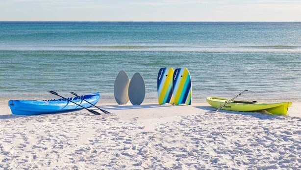 Des kayaks et des planches à pagaie étaient alignés sur une plage de sable, avec l’océan en toile de fond.