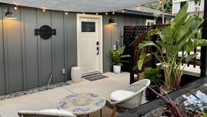 Une terrasse dotée d’un espace salon couvert, d’une porte et d’un petit jardin agrémenté de plantes en pot.
