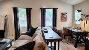 A modern room with a sofa, a desk, and a chair. There is a window with curtains, a stop sign outside, and a garage service sign on the wall.