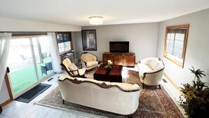 Una sala de estar con sofá, sillones, una mesa de centro, televisor y un ventanal con persianas.